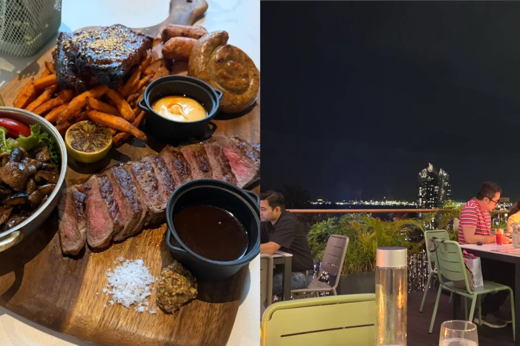 This image highlights a rustic and social dining atmosphere. On the left, a large wooden platter is laden with a feast including a sliced medium-rare steak, sweet potato fries, roasted sausages, a spiral sausage, and sautéed mushrooms. Small black ramekins hold dipping sauces, and a pile of flaky sea salt sits ready for seasoning. On the right, the scene shifts to an outdoor rooftop bar at dusk. Patrons sit at dark tables with light green metal chairs. The background reveals a harbor with twinkling lights and a distinctively modern skyscraper, creating a relaxed, urban evening vibe.