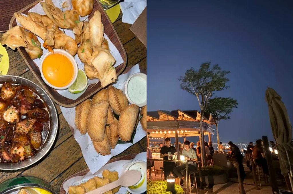 The left side of this image focuses on several plates of golden-brown appetizers served on wooden trays lined with paper. The dishes include crispy wontons with a bright orange dipping sauce, savory empanadas or curry puffs, and a bowl of octopus sautéed in oil and spices. On the right, the rooftop setting is captured during the blue hour of twilight. A large, illuminated outdoor bar is the focal point, surrounded by tall trees and guests seated on high stools. The atmosphere is lively and warm, set against the deep blue transition of the evening sky.