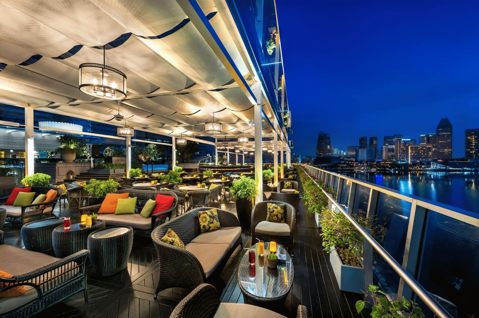 Nighttime rooftop terrace with cozy lounge seating and string lights overlooking a modern city skyline—perfect setting for a Singapore rooftop bar feature.