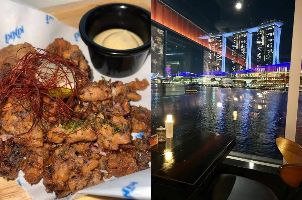 A composite image for a lifestyle feature. The left side is a documentary-style close-up of a plate of crispy, golden-brown fried calamari or octopus, garnished with a nest of thin red chili threads and served on white paper with blue "Kinki" branding. A small black ramekin of creamy dipping sauce sits nearby. The right side captures the evening atmosphere from an indoor dining table, looking through a glass window at the brightly lit Marina Bay Sands and the Singapore waterfront at night.