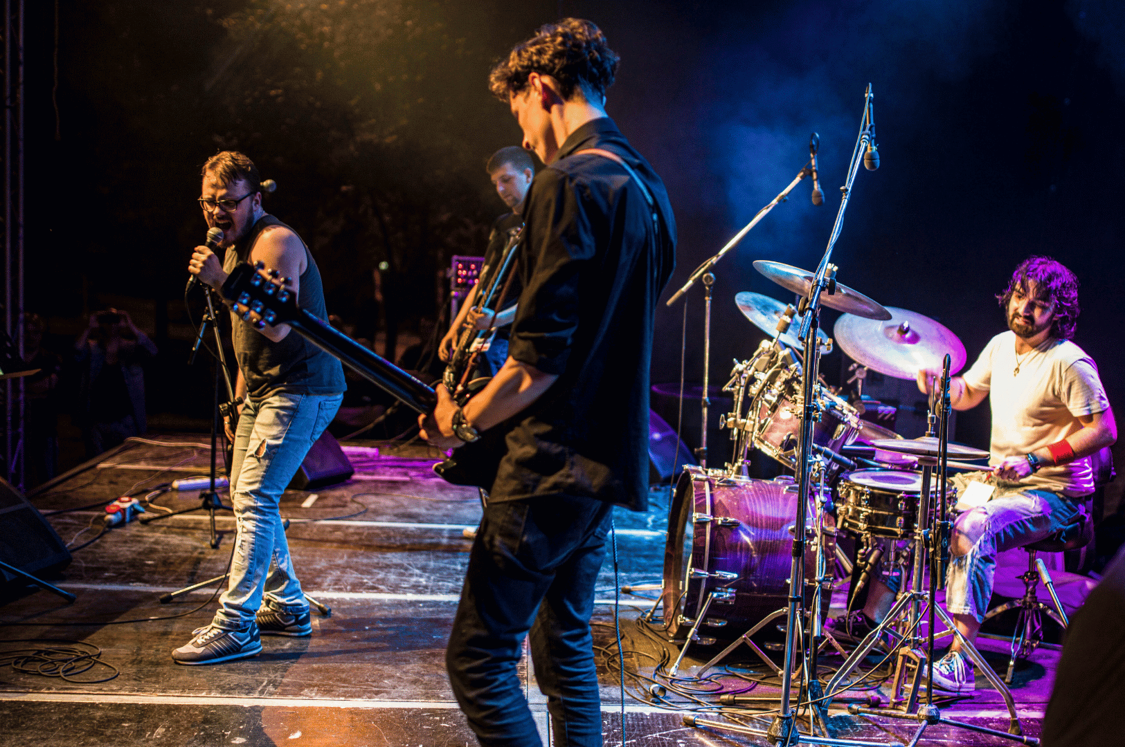 Four-member band performing live on a Singapore stage, with vocalist, guitarist, bassist, and drummer illuminated by vibrant blue and purple lights, showcasing the city’s dynamic local music scene.