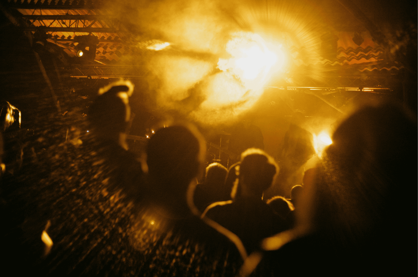 Concert crowd in Singapore silhouetted against dramatic yellow and orange stage lighting with smoke effects, capturing the immersive energy and communal atmosphere of the city’s live music scene.
