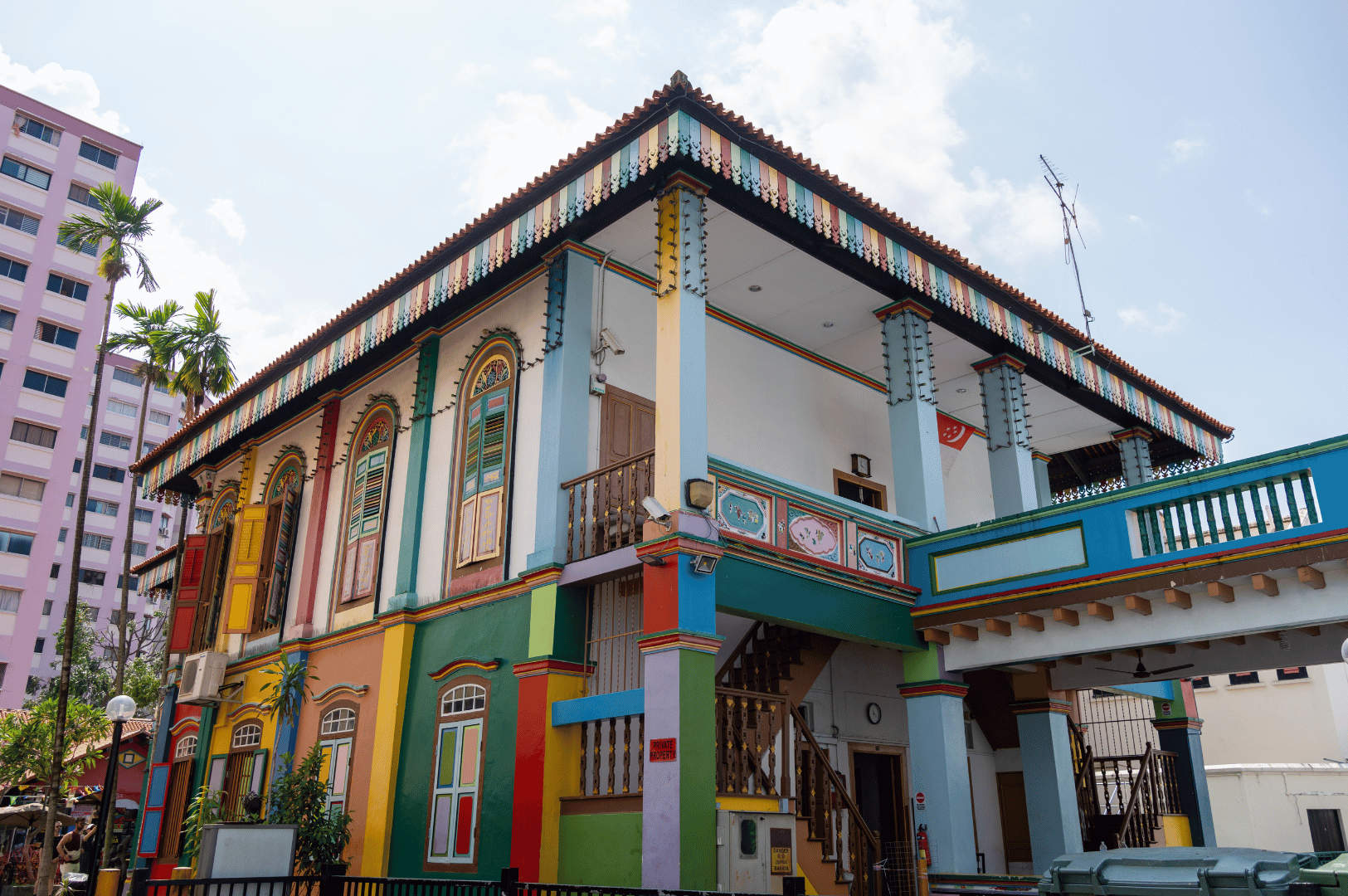 A vibrantly painted heritage shophouse in Singapore with red, green, yellow, and blue details, arched shuttered windows, and ornate trim, set against the backdrop of a modern high-rise—showcasing the city’s blend of tradition and modernity for a weekend itinerary.