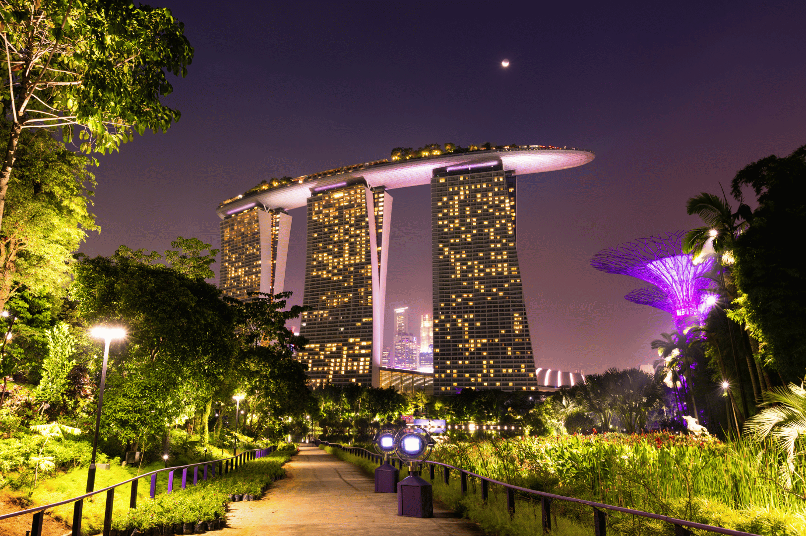 The Marina Bay Sands resort in Singapore illuminated against the night sky, with its three towers connected by a ship-like sky park, and the glowing Supertree Grove in the background—showcasing the city’s futuristic skyline for a weekend itinerary.