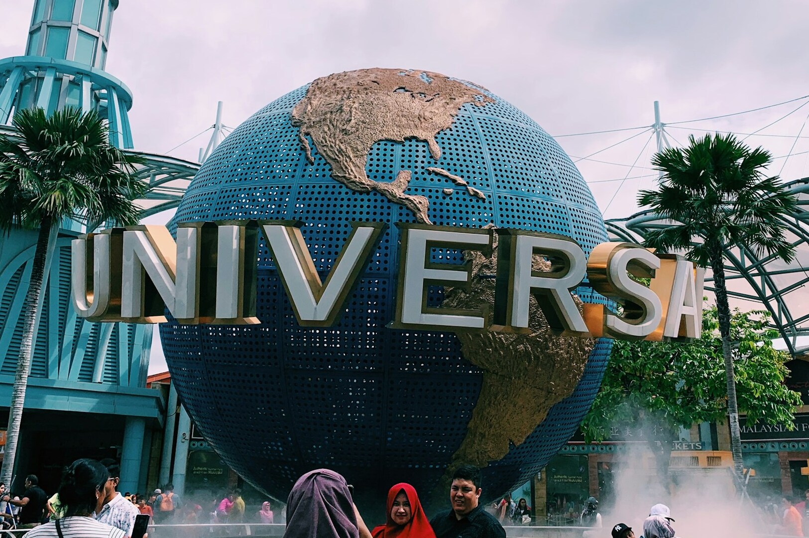 A woman and a man pose in front of a large globe at Universal Studios Singapore, showcasing the park's global theme.