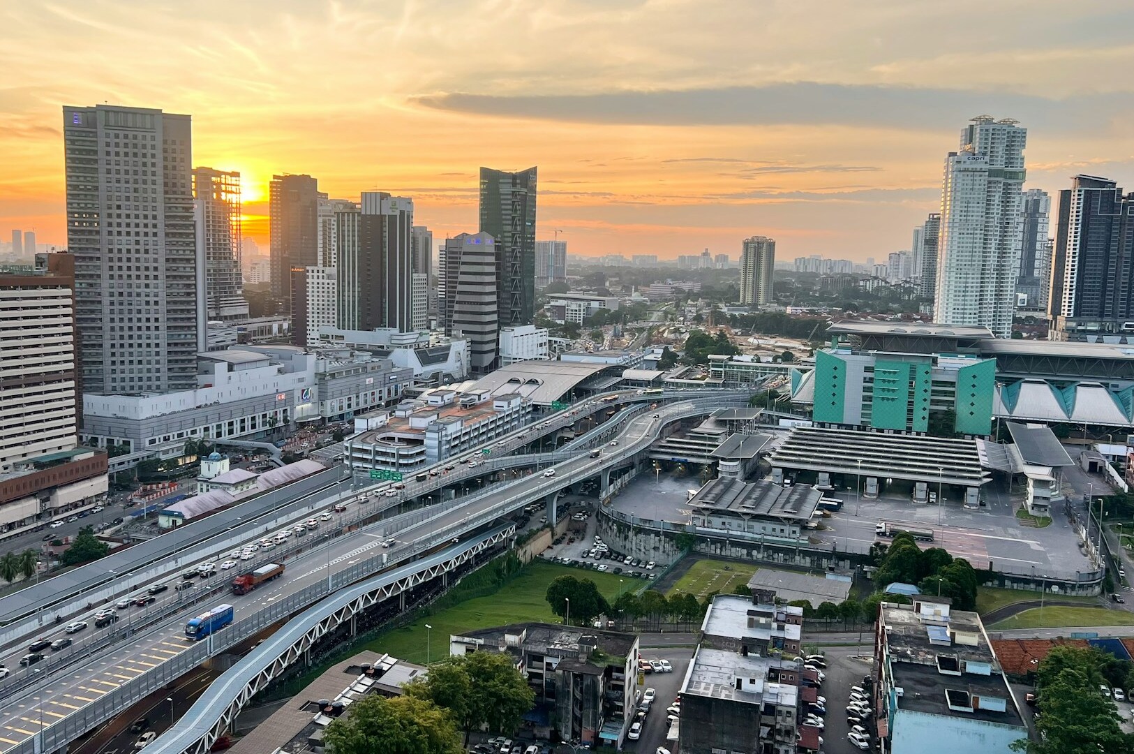 A vibrant sunset paints the skyline of Johor Bahru hotels, with vehicles moving through the bustling city streets.