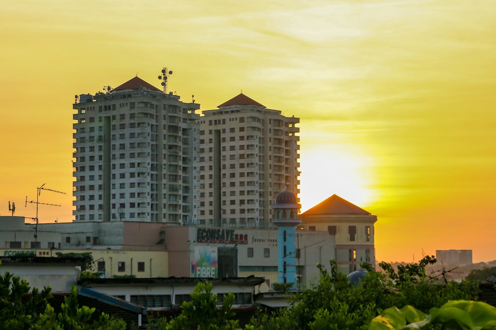 A city skyline at sunset, with tall buildings silhouetted against the colorful sky. Your ideal budget hotel visible.