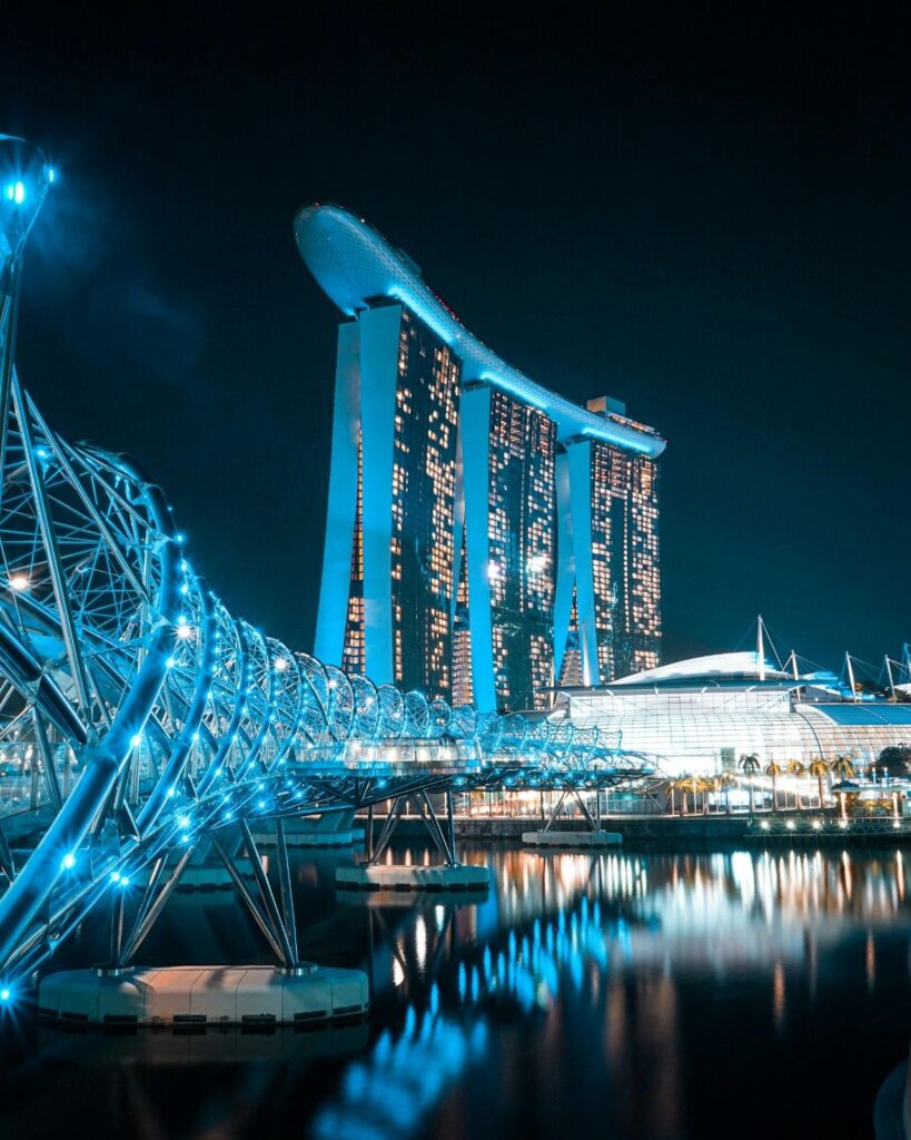 Nighttime view of the illuminated Helix Bridge and Marina Bay Sands hotel reflected in the water, Singapore.