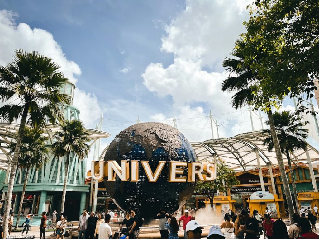 Crowds of tourists visiting Universal Studios Singapore entrance at Sentosa Island with palm trees and blue sky.