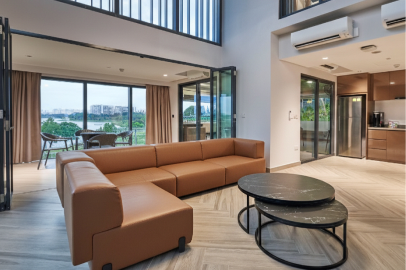 Modern living room with a tan L-shaped sofa, marble nesting coffee tables, and a large balcony overlooking a reservoir.