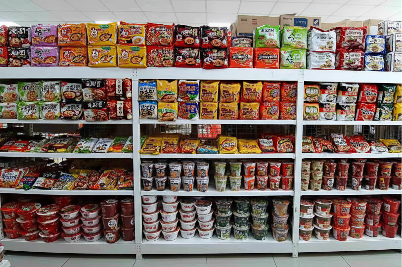Neatly organized shelves in a grocery store filled with various brands of Korean instant ramen in both packets and cups.
