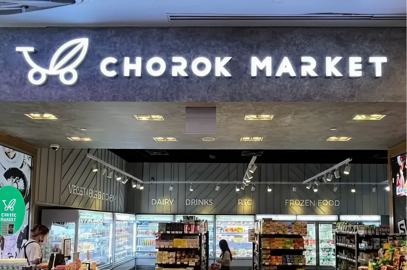 he modern storefront of "Chorok Market" with bright signage above glass-door refrigerators labeled Dairy, Drinks, and Frozen Food.