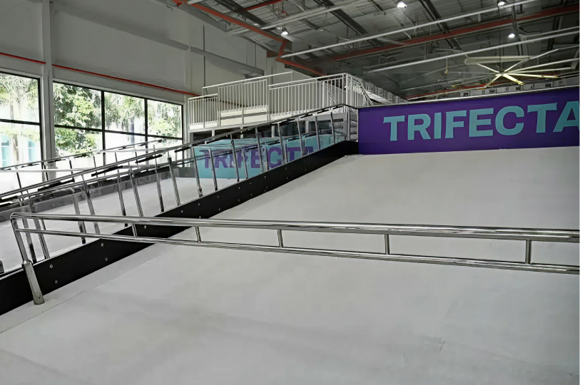 An indoor snowboarding and skiing simulator featuring a white revolving slope and silver safety railings.