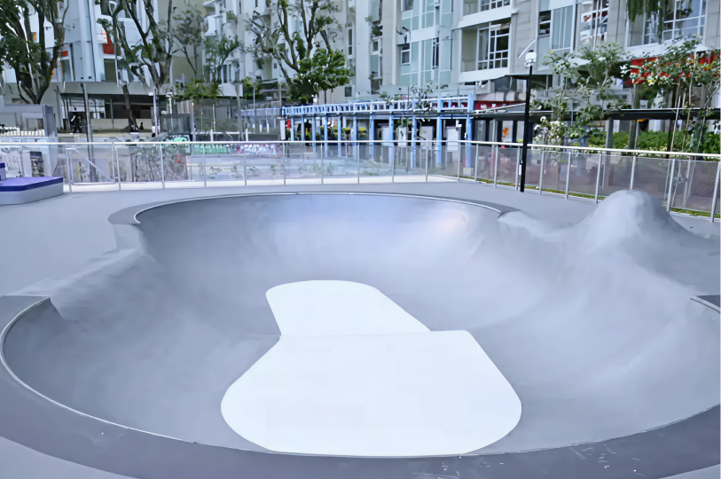 An outdoor gray concrete skate bowl and pump track designed for skateboarding and surf-skating.