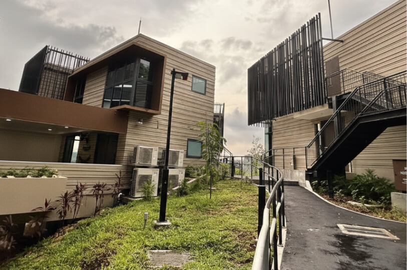 A paved walkway winding through landscaped grass between modern multi-story villa units with unique architectural finishes.