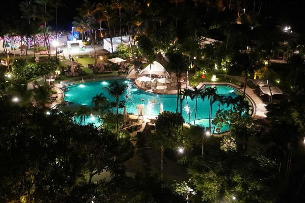 Nighttime aerial view of a Sentosa resort, highlighting luxury hotels with private pools and vibrant lighting.