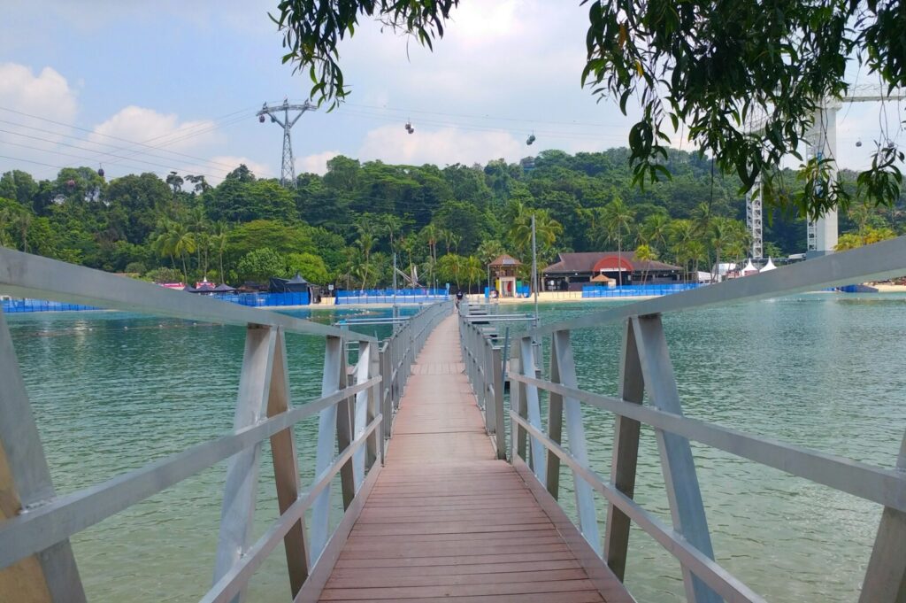 A scenic wooden walkway extends to a lake featuring a water park, highlighting the future of Sentosa hospitality.