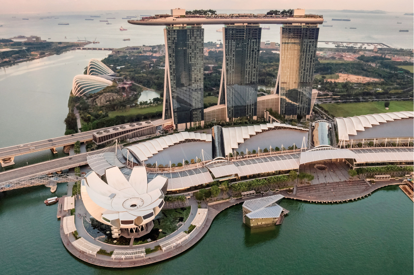 An aerial view of the Marina Bay Sands resort in Singapore, featuring three iconic skyscrapers topped by a boat-shaped sky park, situated next to the lotus-shaped ArtScience Museum and the waterfront.