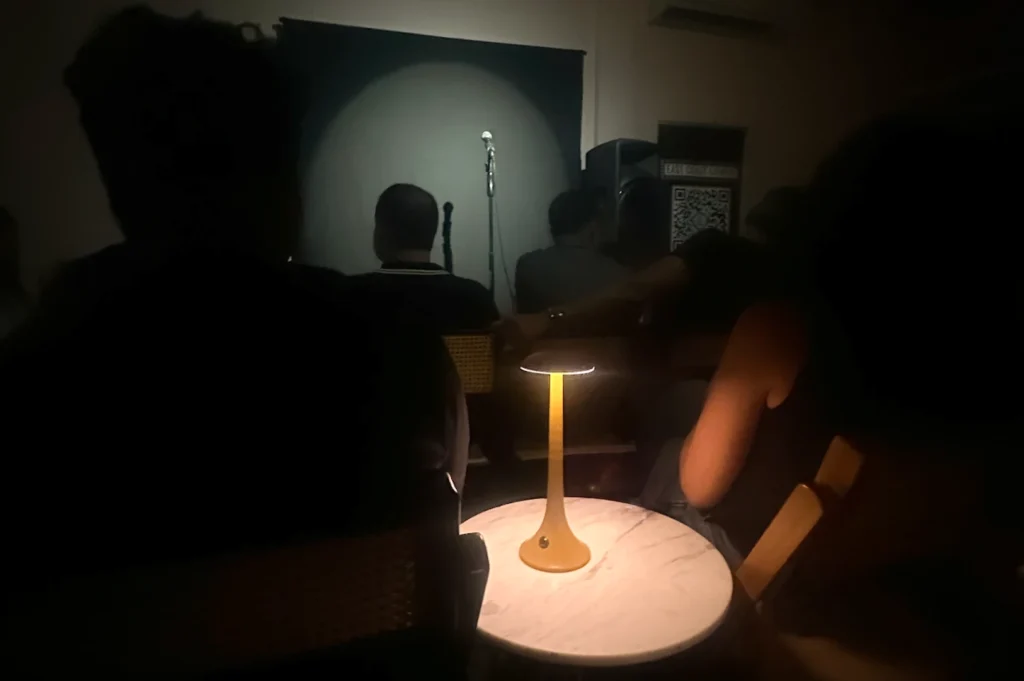 The intimate interior of East Coast Comedy in Singapore, showing a darkened room with an audience seated at tables and a microphone illuminated by a spotlight on stage in the background.