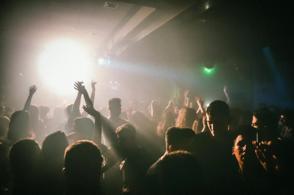 Crowded nightclub dance floor with people dancing under bright stage lights and smoky atmosphere during a late-night party event