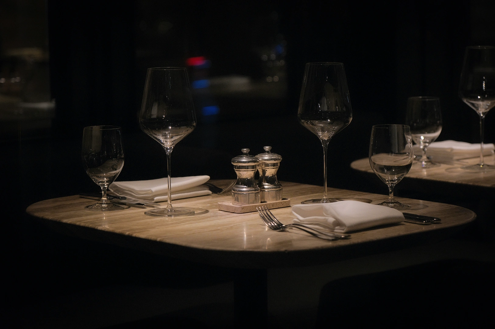 Elegant fine dining table setting with wine glasses, folded white napkins, silverware, and salt and pepper shakers on a dimly lit restaurant table.