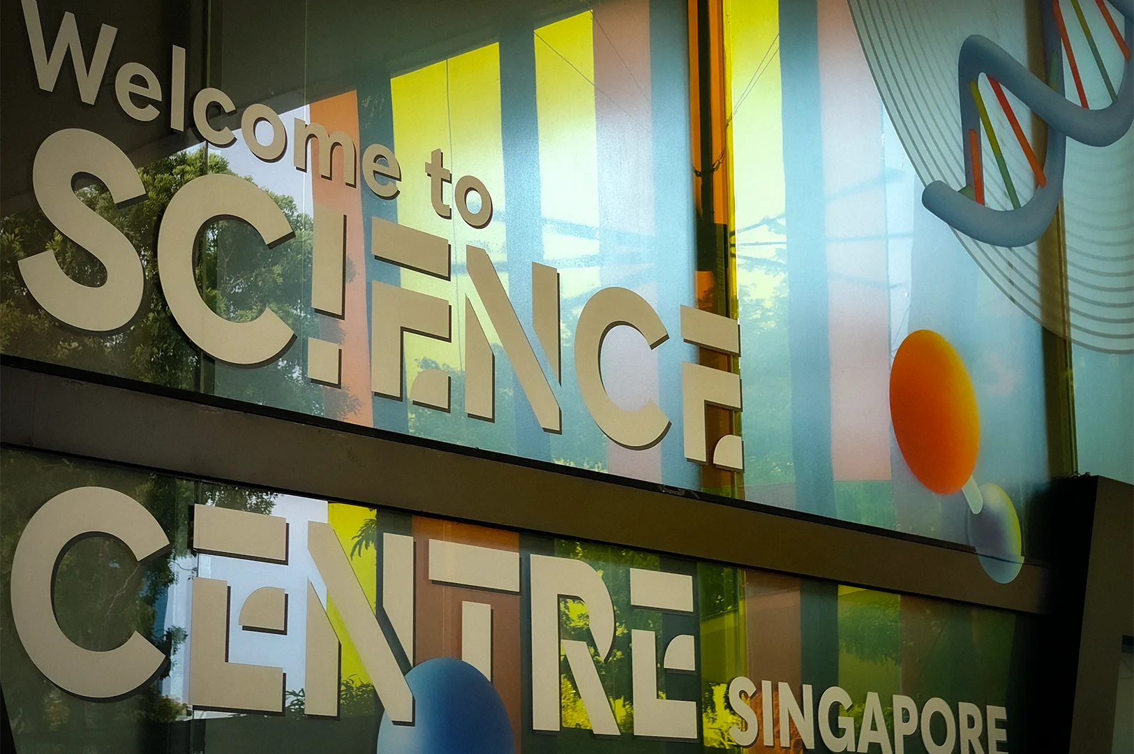 Welcome to Science Centre Singapore sign displayed on colorful glass panels with modern scientific-themed graphics at the attraction entrance in Singapore