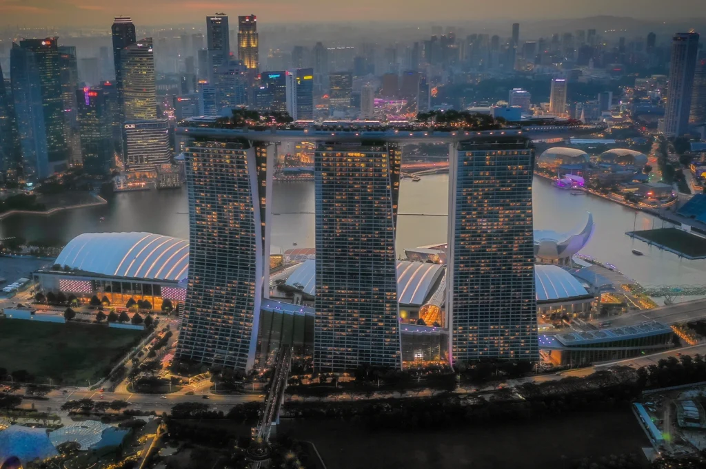 Aerial sunset view of the Marina Bay Sands hotel and Singapore city skyline overlooking the water.