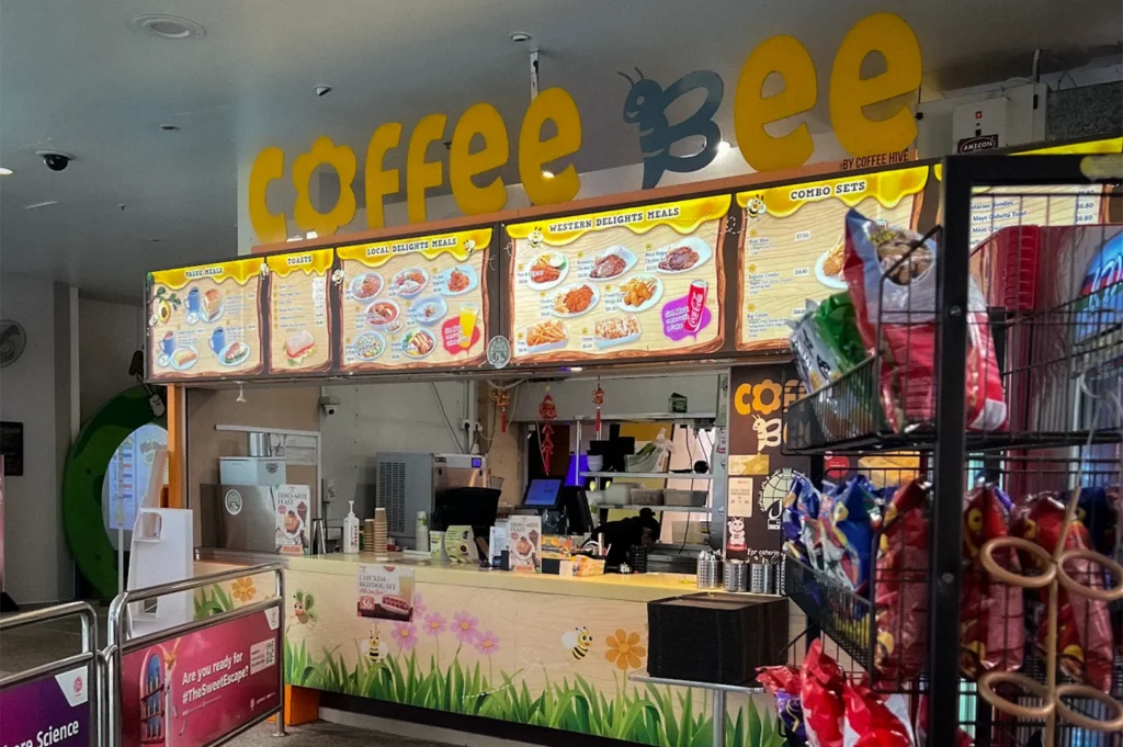 Coffee Bee snack and beverage kiosk inside Science Centre Singapore featuring colorful menu boards, packaged snacks, and casual dining counters for visitors and families
