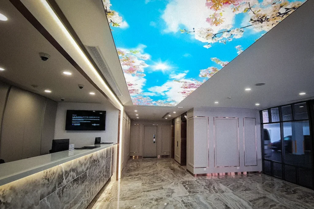 Elegant lobby interior at Hotel 81 Palace Singapore featuring marble flooring, a modern reception desk, recessed lighting, and a decorative floral ceiling display with blue sky artwork