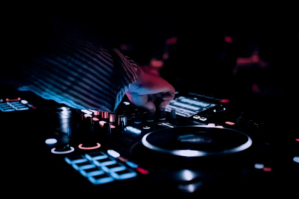 Close-up of a DJ mixing music on a professional controller with illuminated buttons and knobs in a dark nightclub setting