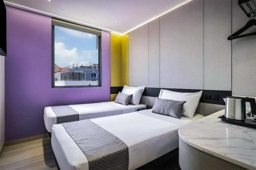 Twin room at Hotel 81 Palace Singapore featuring two single beds, modern minimalist decor, purple accent wall, LED ceiling lighting, and a compact marble-top desk area