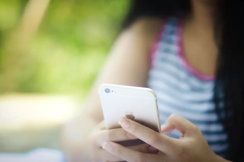Close-up of a person holding and using a smartphone outdoors, with a blurred background of greenery.