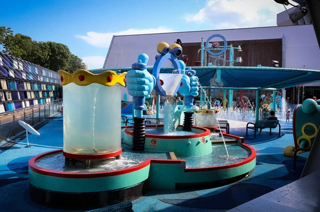Colorful outdoor Waterworks play area at Science Centre Singapore featuring interactive water fountains, splash structures, shaded seating, and family-friendly attractions on a sunny day
