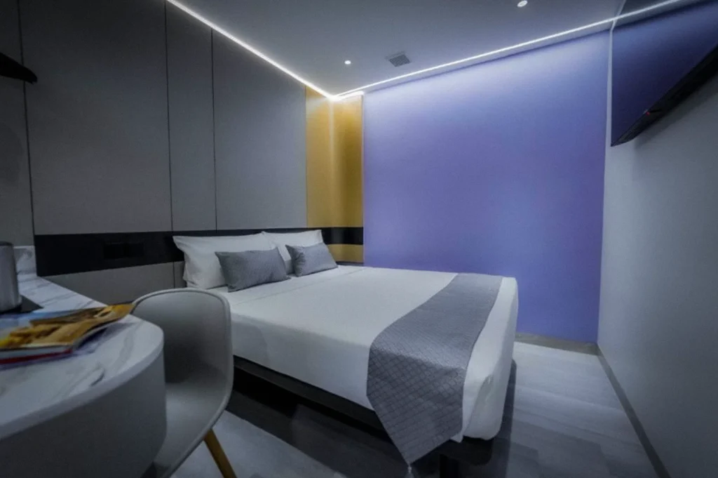 Modern guest room interior at Hotel 81 Palace Singapore featuring a queen-size bed, minimalist decor, soft LED lighting, and a purple accent wall