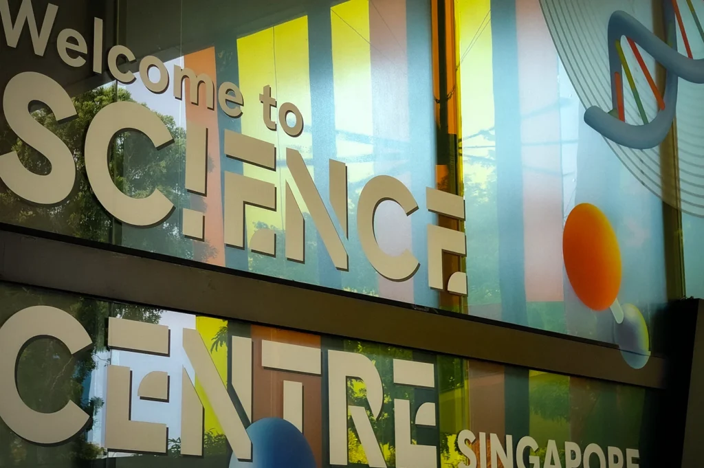 Colorful Science Centre Singapore entrance sign on glass windows featuring modern graphics and DNA-themed artwork outside the attraction building