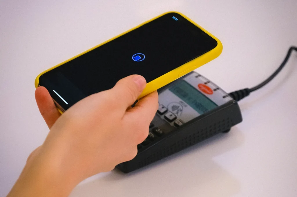 Customer making a contactless mobile payment by tapping a smartphone on a card payment terminal, demonstrating digital wallet and NFC payment technology at a checkout counter.