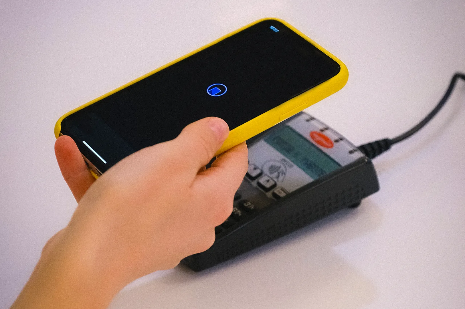 Customer making a contactless mobile payment by tapping a smartphone on a card payment terminal, demonstrating digital wallet and NFC payment technology at a checkout counter.