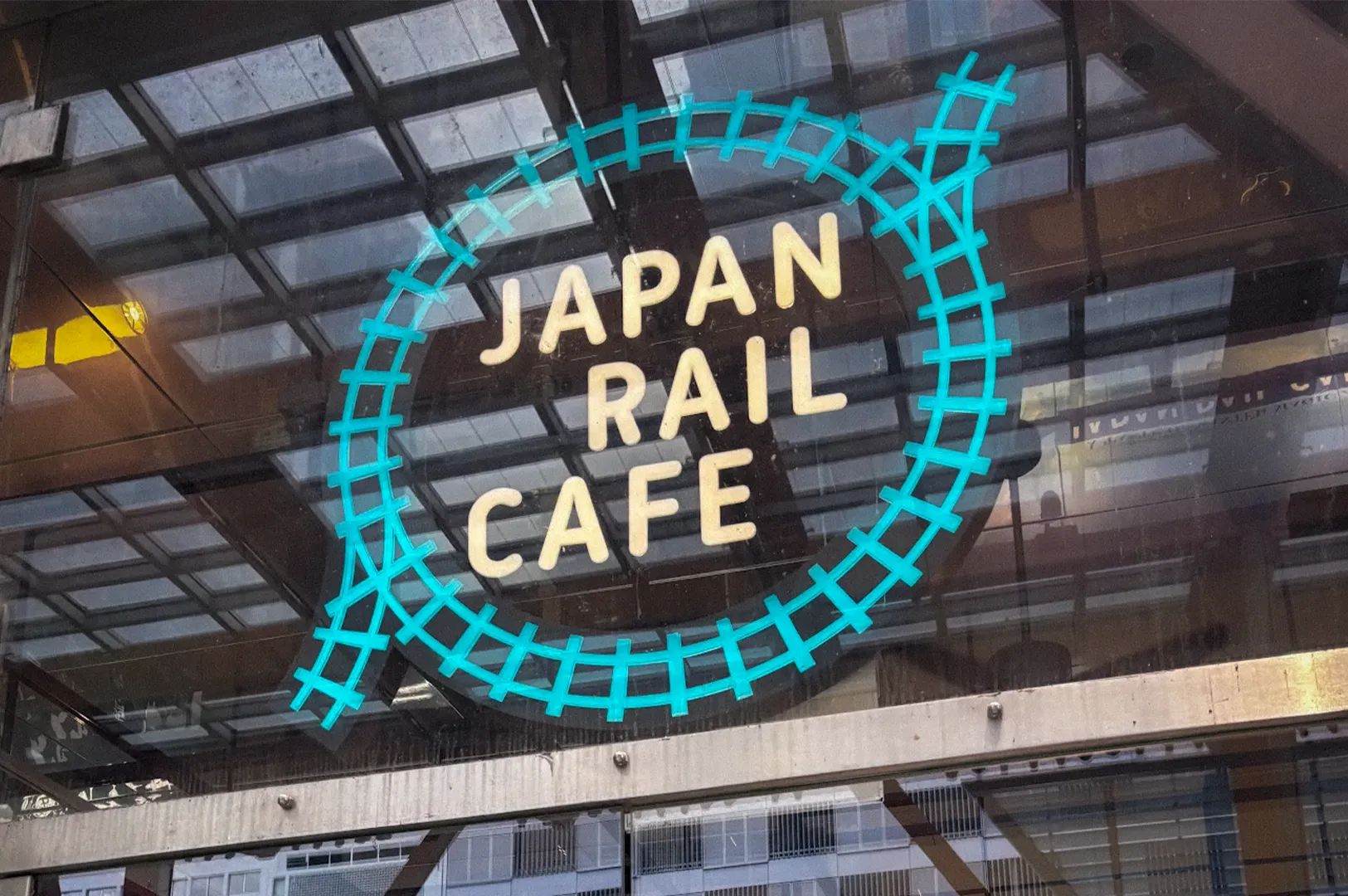 Japan Rail Cafe Singapore storefront featuring the iconic railway-inspired logo on a glass facade, with cafe entrance, retail displays, and Japanese travel-themed branding visible from the street.