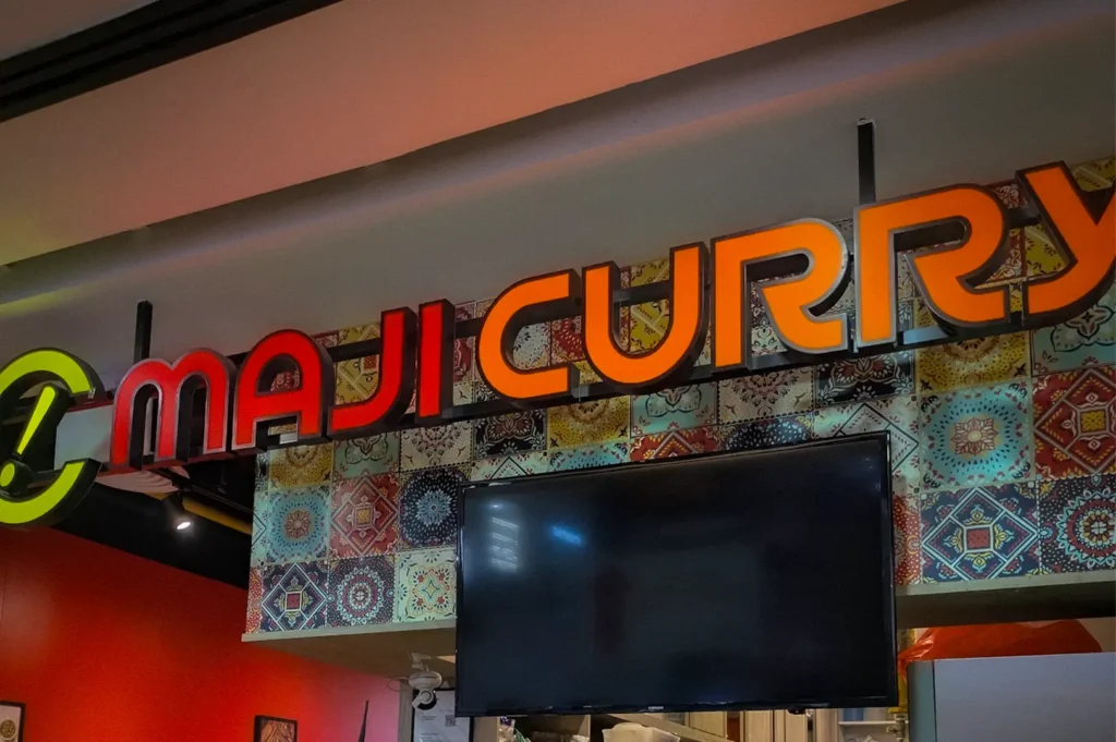 Maji Curry restaurant counter in Singapore featuring self-order kiosks, illuminated signage, menu displays, and staff preparing authentic Japanese curry dishes.