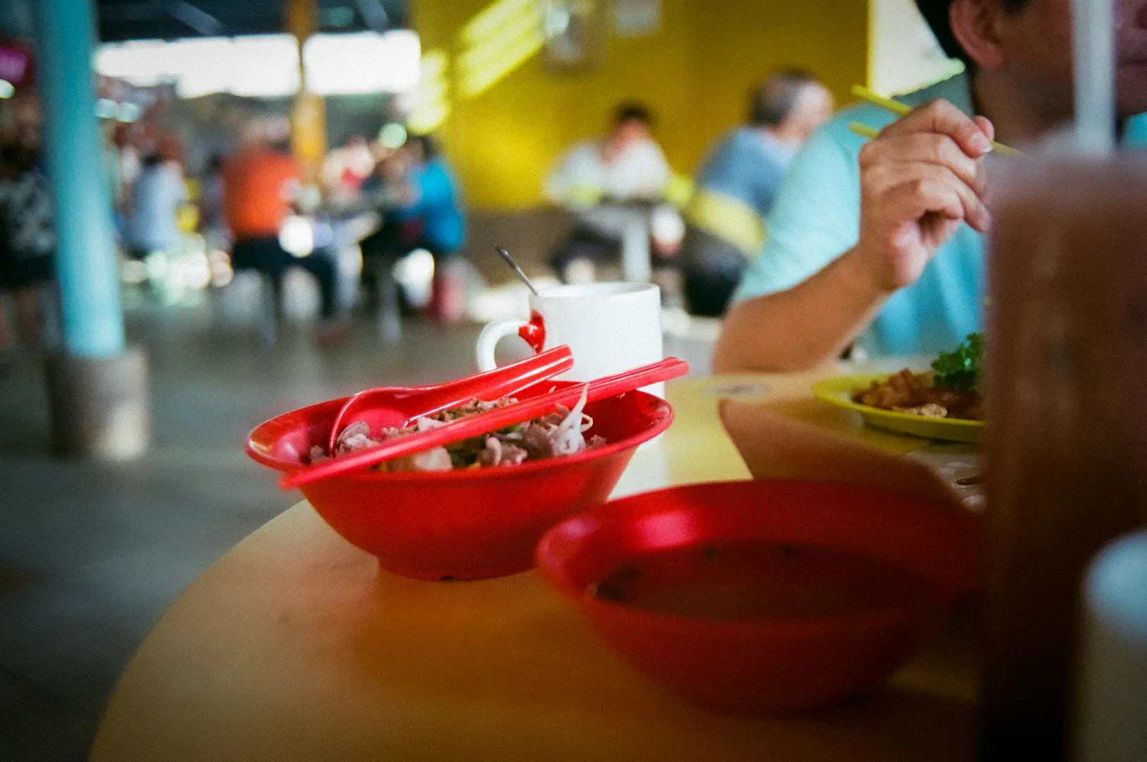 People dining at a Singapore hawker centre with local food dishes, communal seating, and a bustling food court atmosphere.