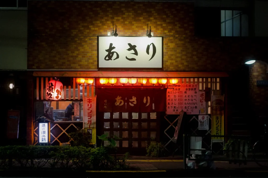 Traditional Japanese izakaya restaurant exterior in Gotanda, Tokyo at night with glowing red lanterns, Japanese signage, and cozy street atmosphere