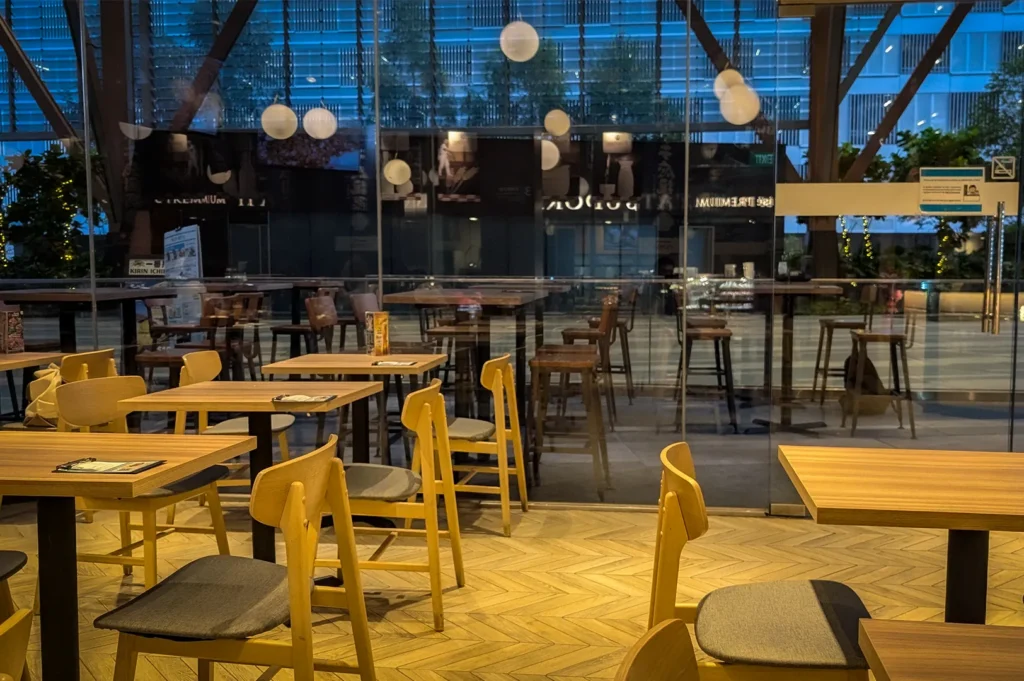Interior dining area of Japan Rail Cafe Singapore featuring modern wooden tables and chairs, floor-to-ceiling glass windows, warm lighting, and a spacious Japanese-inspired cafe atmosphere.