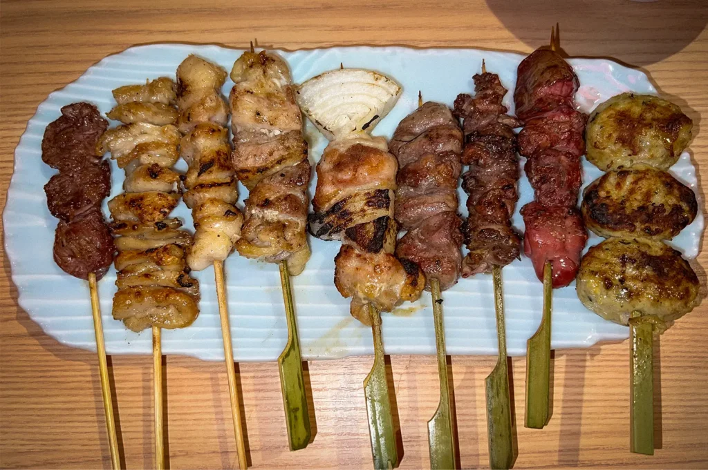 Assorted Japanese yakitori skewers served on a rectangular plate in Singapore, featuring grilled chicken, beef, pork, chicken liver, onion, and tsukune meatballs.