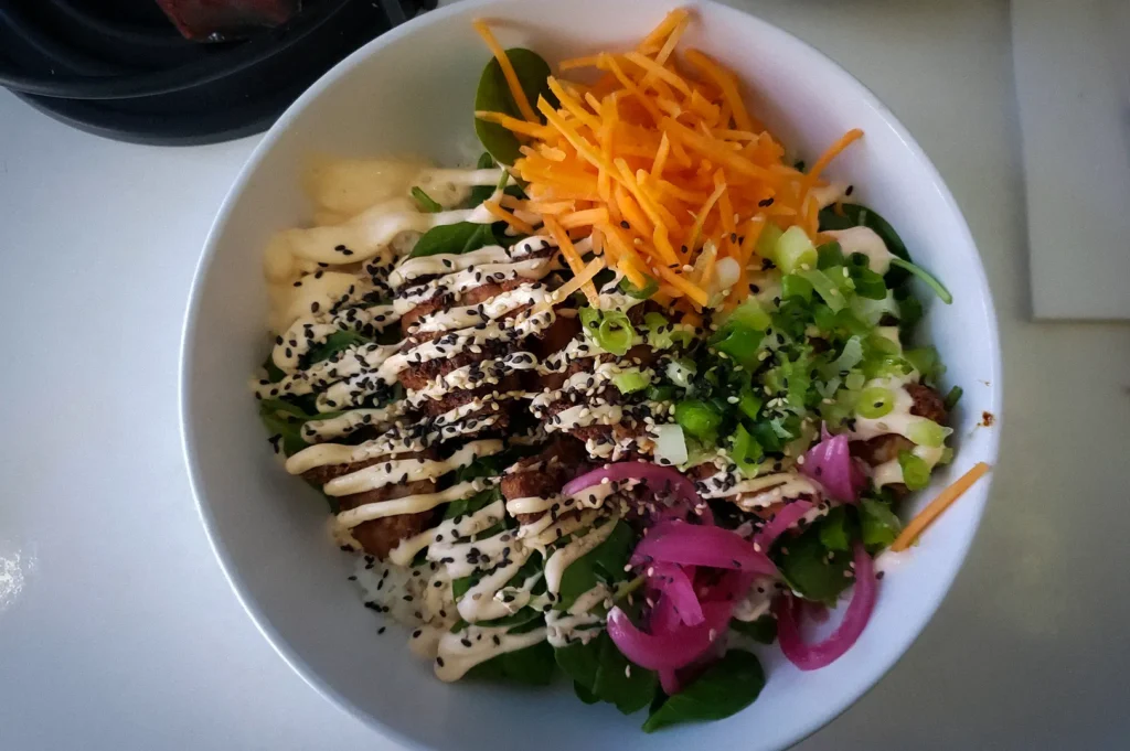 Japanese chicken karaage rice bowl in Singapore topped with crispy fried chicken, pickled onions, shredded carrots, spring onions, sesame seeds, and creamy mayo over fresh greens.