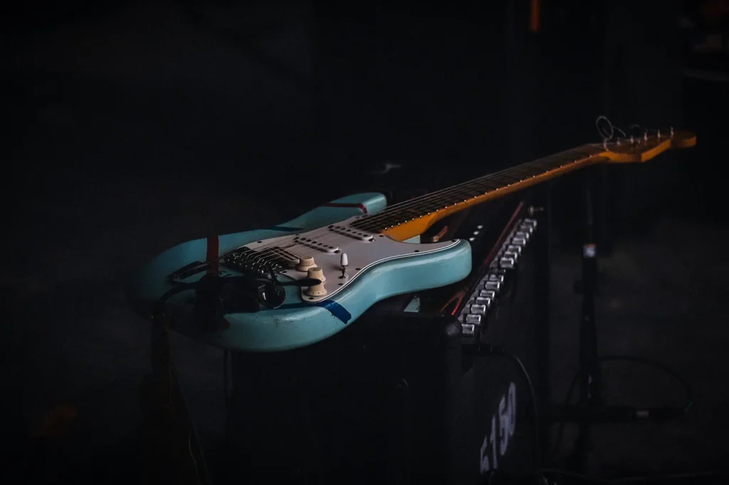 Close-up of an electric guitar resting on an amplifier in a dimly lit live music venue. The stage setup highlights professional musical equipment and creates an intimate atmosphere for live performances, acoustic sessions, and local band events.