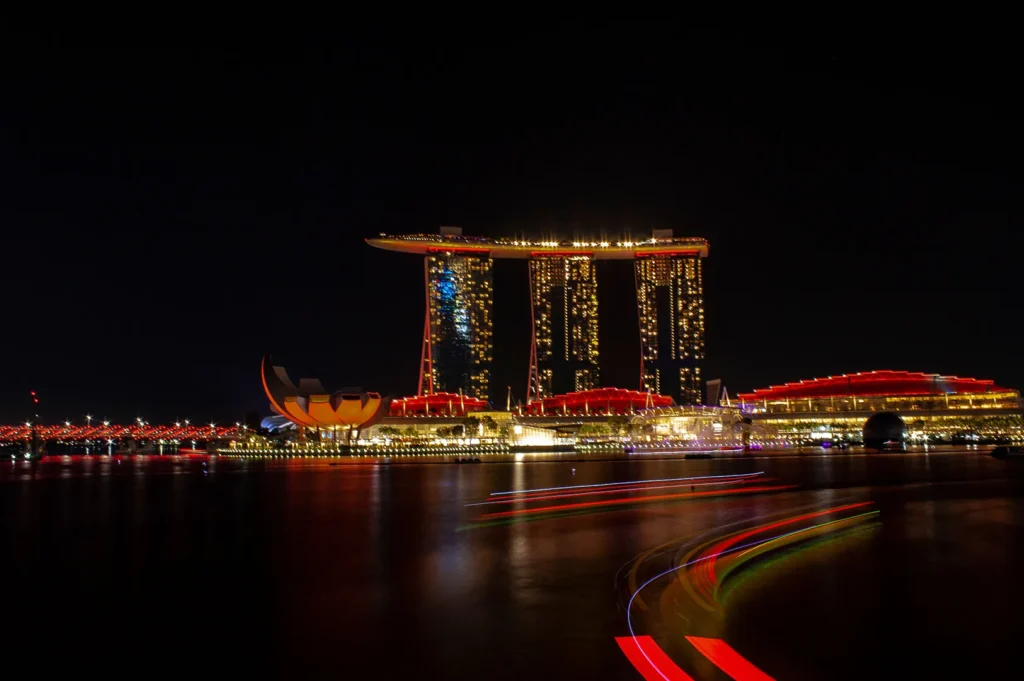 Marina Bay Singapore illuminated at night with Marina Bay Sands, ArtScience Museum, and waterfront reflections. Long-exposure light trails from passing boats create a vibrant cityscape showcasing Singapore’s iconic skyline and attractions.