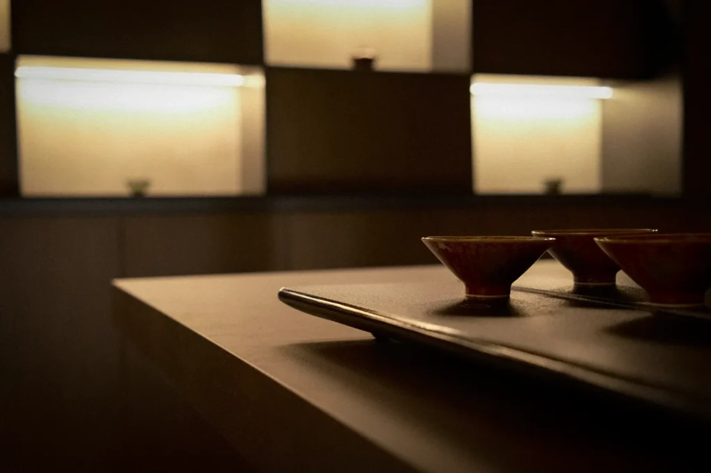 Traditional Chinese teacups displayed on a tea table inside Tea Room by Ki-Setsu at Orchard Plaza, Singapore. Warm ambient lighting, wooden interiors, and minimalist tea room design create a serene atmosphere for tea appreciation and tea ceremonies.