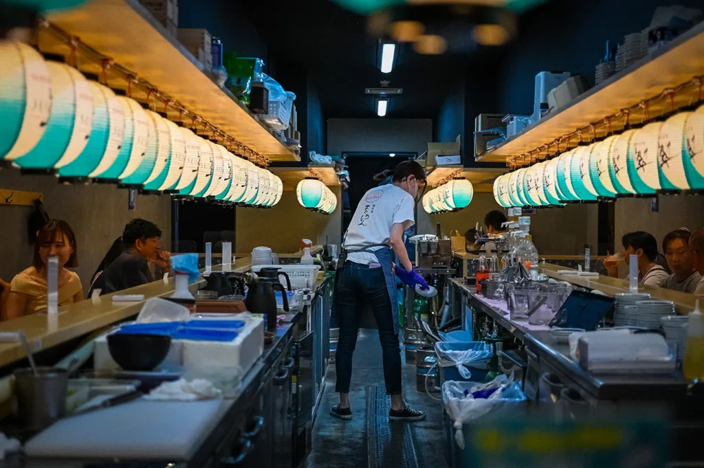 Japanese-style izakaya restaurant in Singapore with illuminated paper lanterns, open counter seating, chefs preparing food, and a lively casual dining atmosphere.