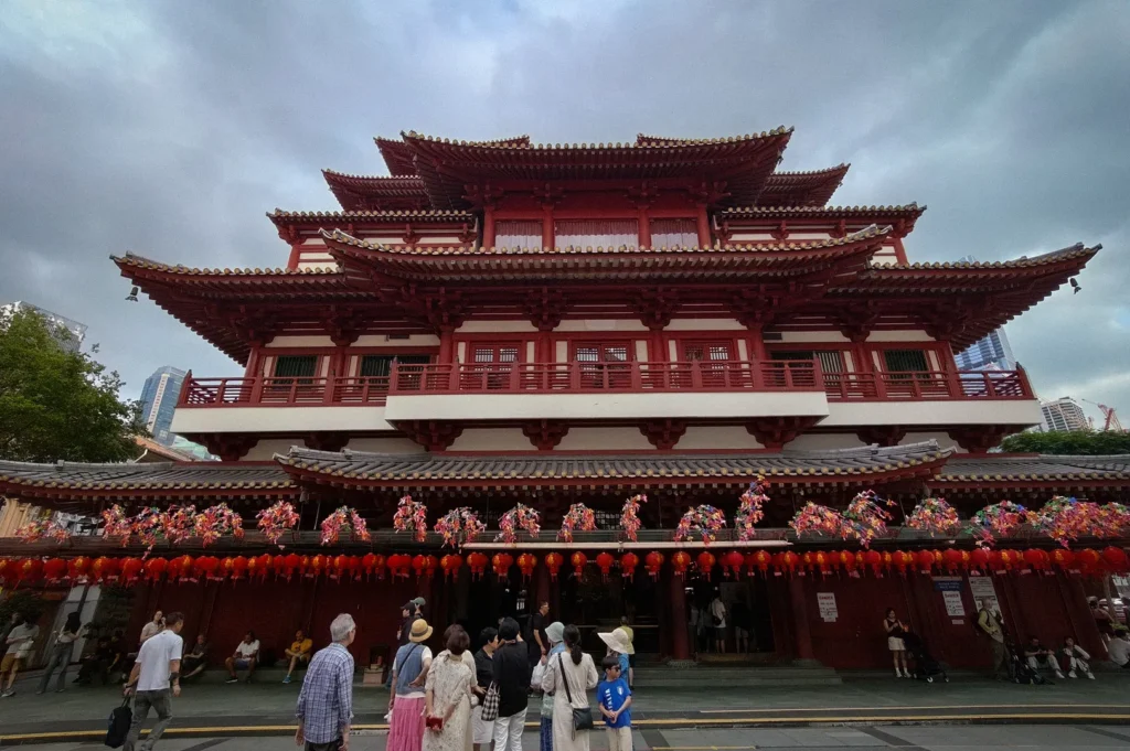Front view of the Buddha Tooth Relic Temple in Singapore’s Chinatown, showcasing traditional Tang-style architecture, red lanterns, ornate tiered roofs, and visitors gathered at the temple entrance.
