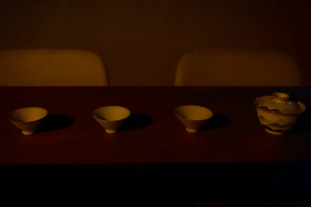 Traditional Chinese tea cups and a porcelain gaiwan arranged on a wooden tea table at Tea Room by Ki-Setsu in Orchard Plaza, Singapore. Elegant teaware is prepared for an authentic Chinese tea tasting and tea appreciation session in a serene tea room setting.